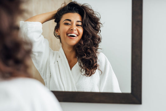 Woman with curly hair standing infront of the mirror and laughing