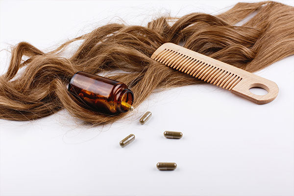 comb and vitamin bottle placed on top of hair extensions