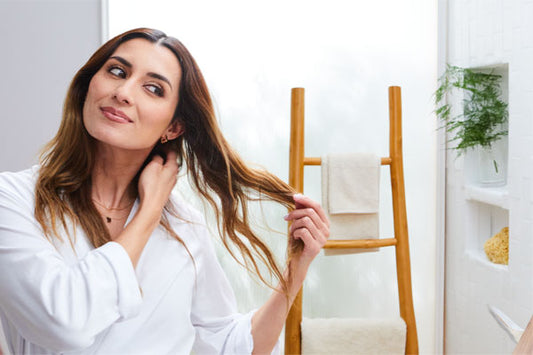 Woman in a white shirt gently touches her long hair, smiling slightly. 