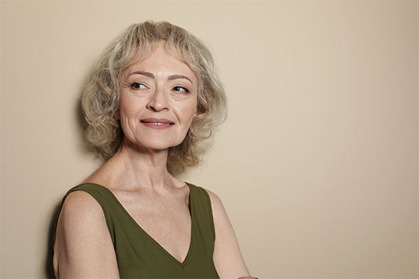 Woman with short hair and green top standing against a beige wall
