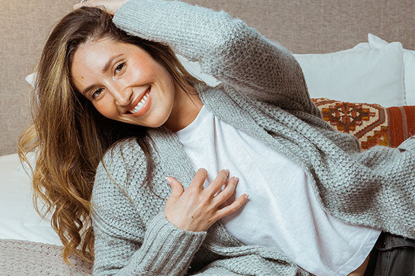 Woman in grey sweater laying on bed and smiling