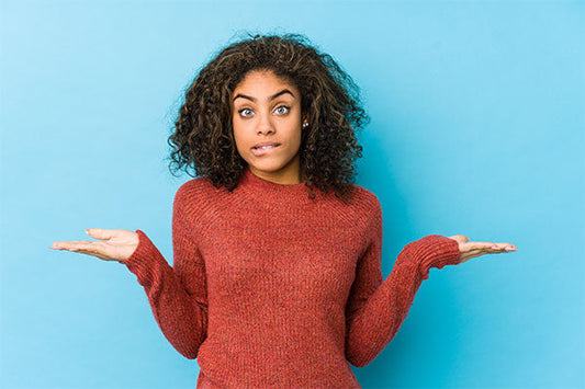 A woman with black curly hair and red sweater shrugging