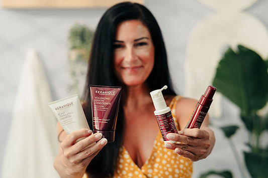 A woman with long dark hair holding keranique hair products