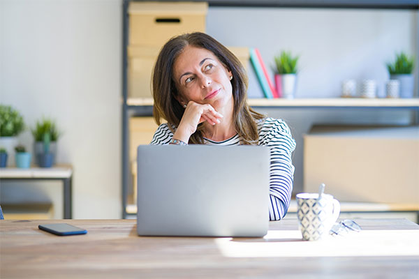 Woman sitting on the desk in front of a laptop with a thoughtful expression