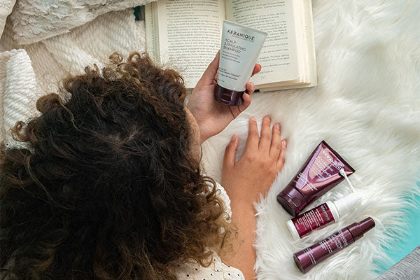 woman laying in bed looking at keranique hair products