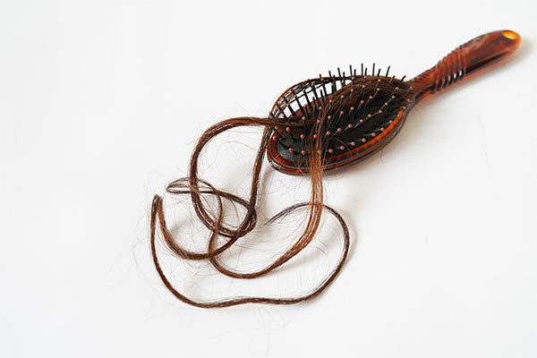 A brush with brown hair strands stuck on it 