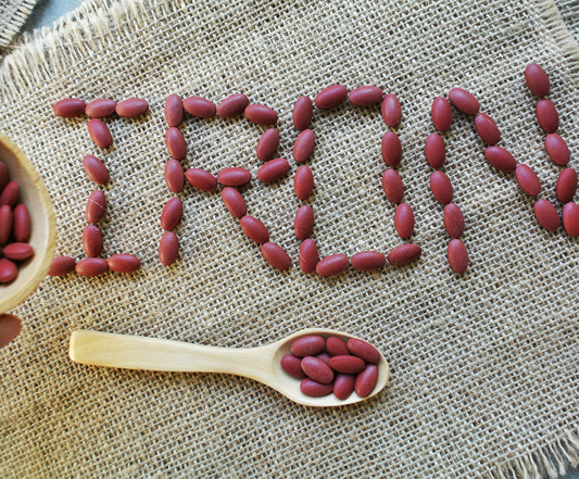 "Iron" spelled out with red pills with a wooden spoon placed below the word 